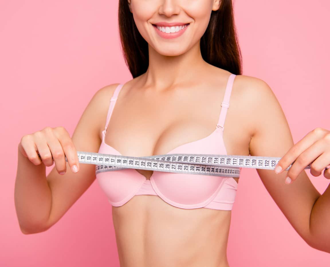 Cropped close-up photo of nice cute adorable attractive cheerful positive optimistic girl in beige bra measuring chest size line with tape isolated over pink background