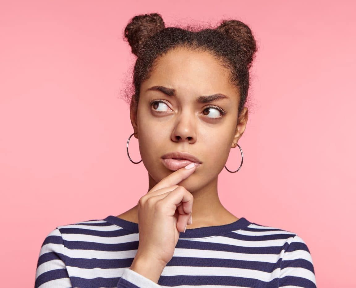 Pensive female thinks about solving her problem, tries to predict all possible ways out, looks aside, poses against pink background