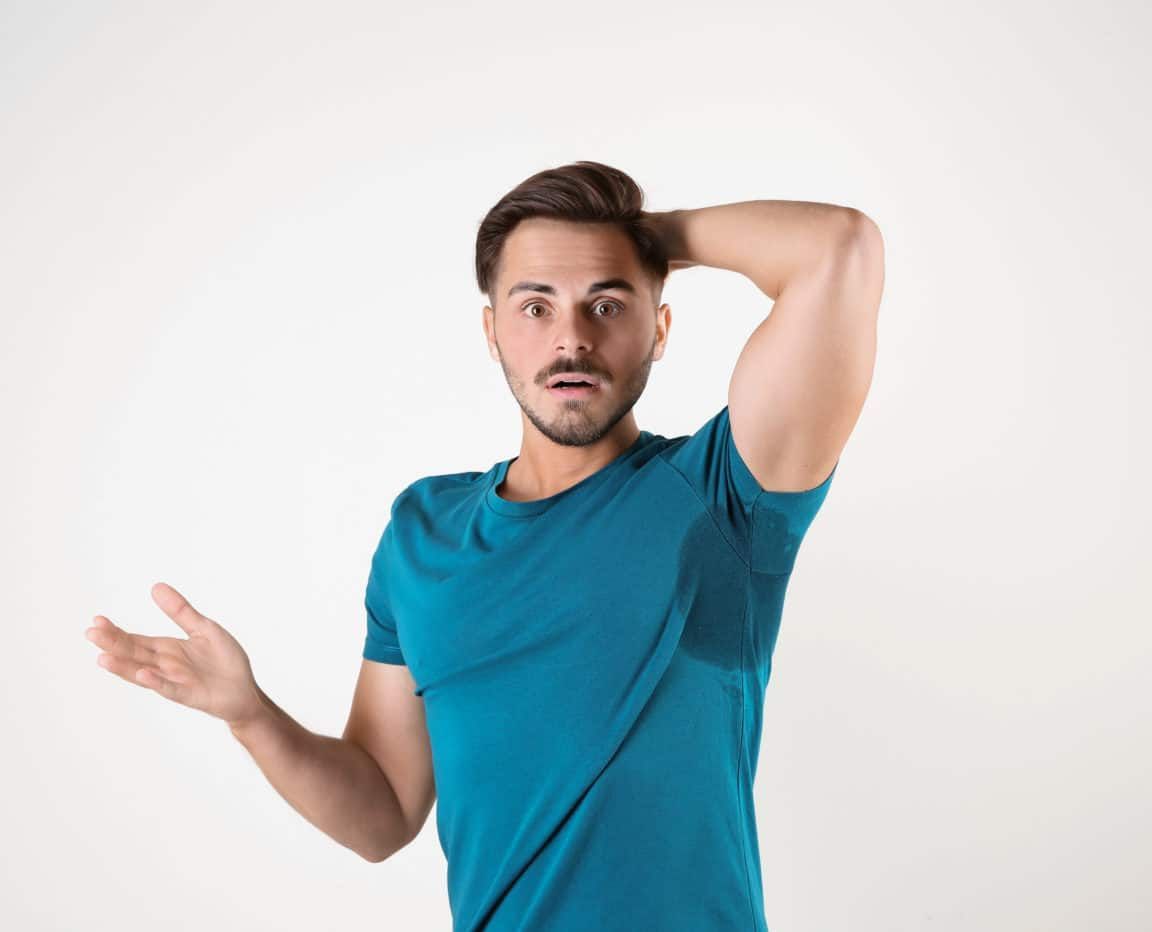 Sweaty man with stain on t-shirt against white background. Using deodorant