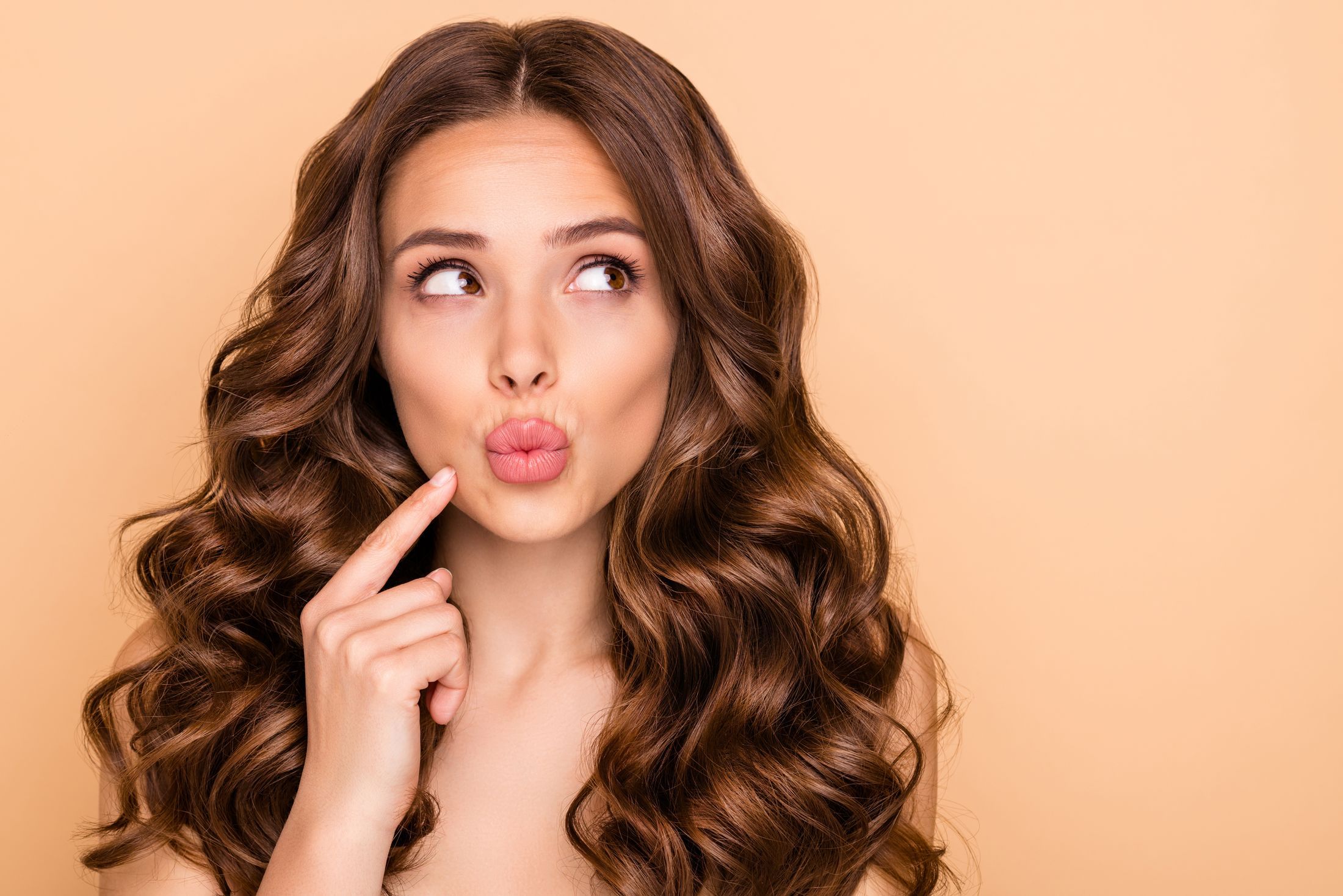 Pensive wavy-haired woman thinking looking aside pouted lips isolated over beige pastel color background