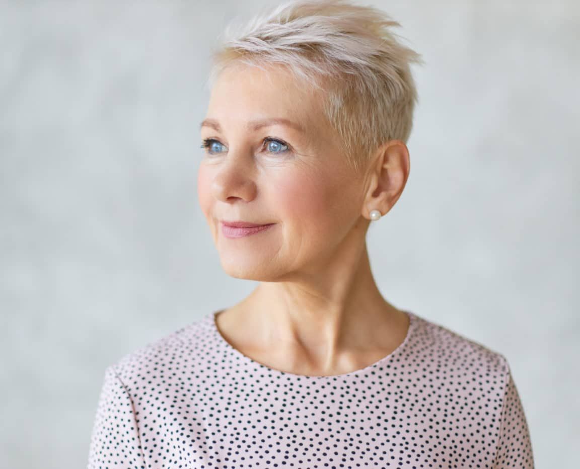 Close up studio image of beautiful attractive middle aged European lady with stylish haircut and neat make up looking away with confident smile posing isolated against marbled wall background